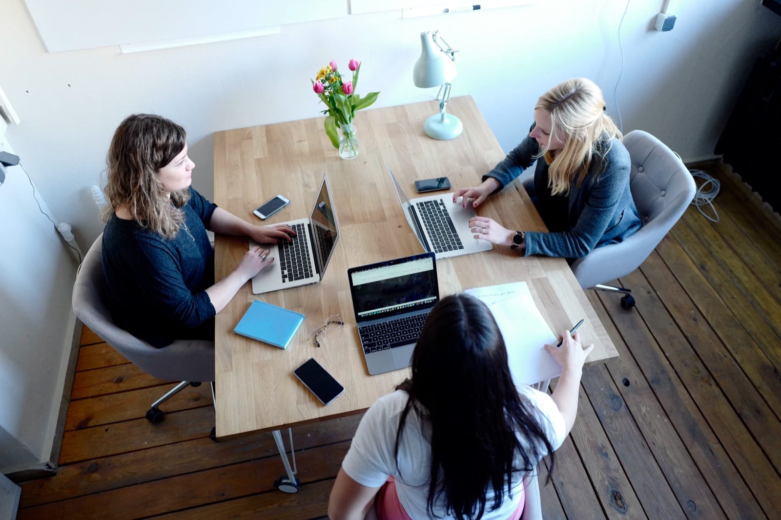 Drie collega’s overleggen rond een tafel met laptops