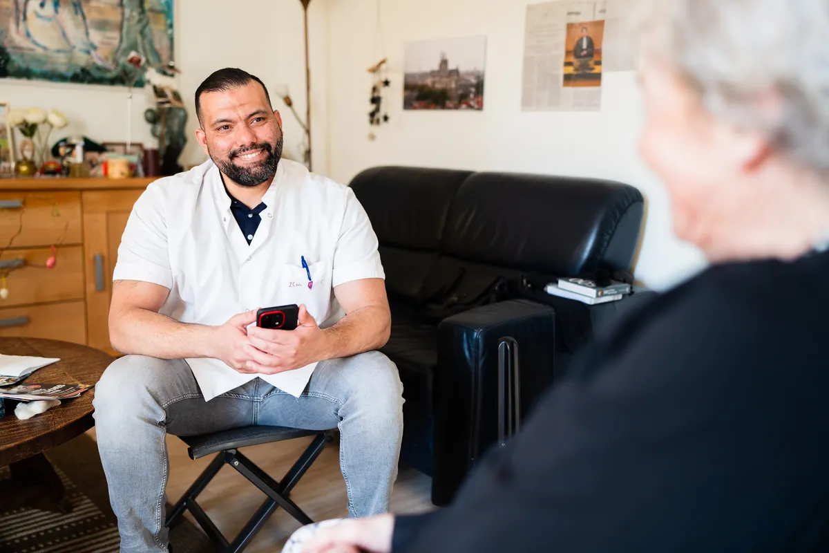 Een verpleegkundige met zijn telefoon, in gesprek met een bewoner