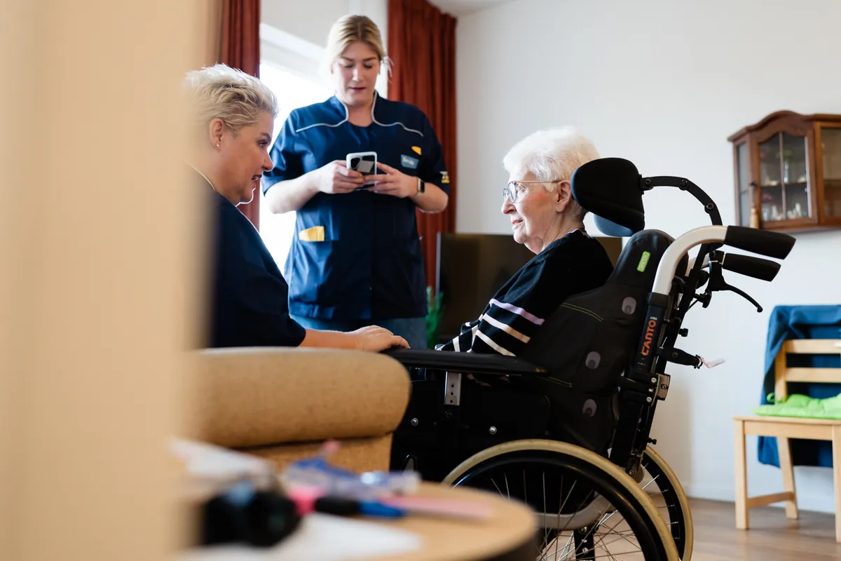 Een zorgteam aan het werk, bij een bewoner in een rolstoel